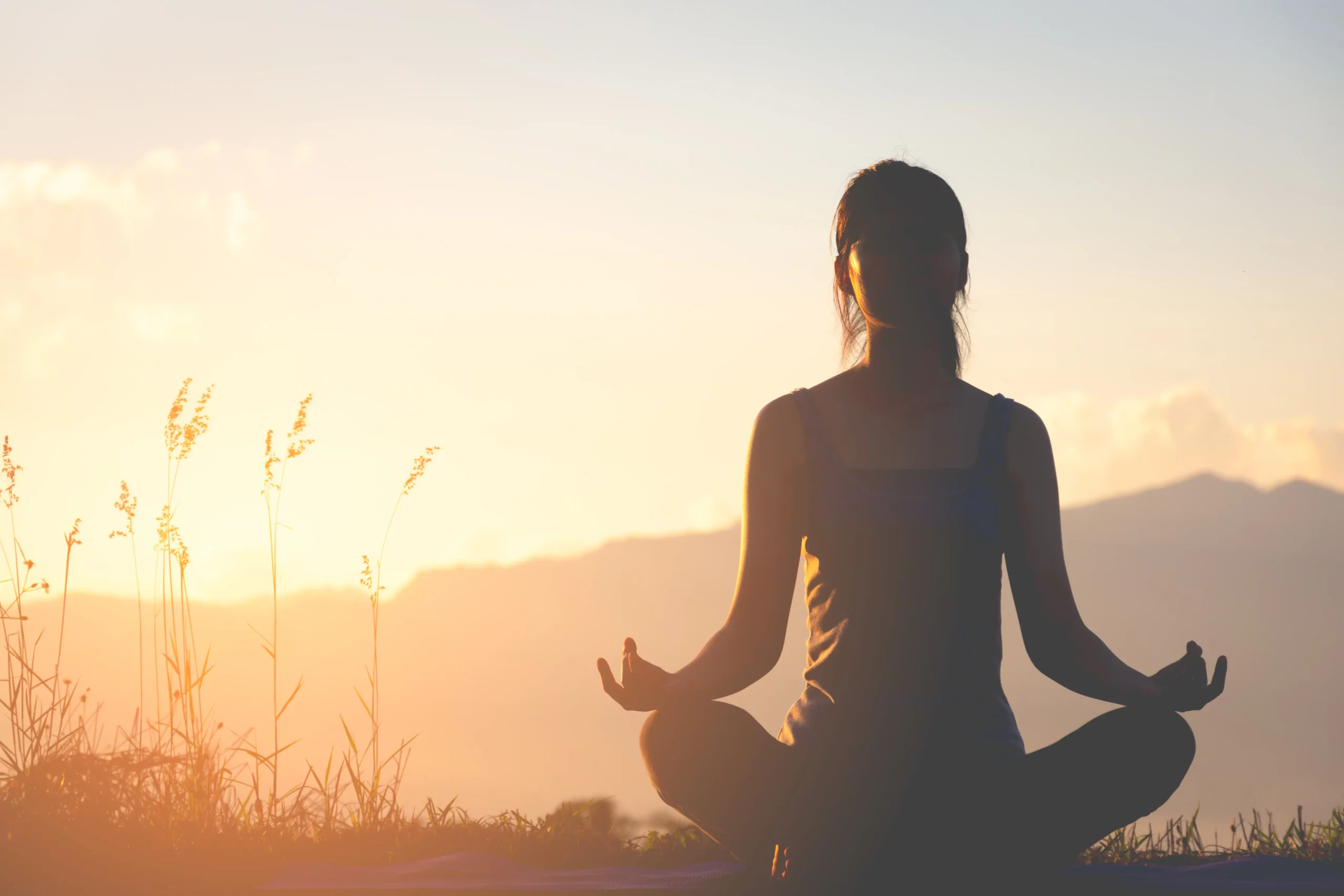 A Silhouette of a girl racticing yoga with a mountain in the background with the sun rising from behind it.